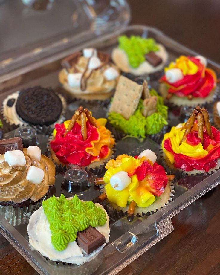 cupcakes with colorful frosting and toppings in a plastic container on a wooden table