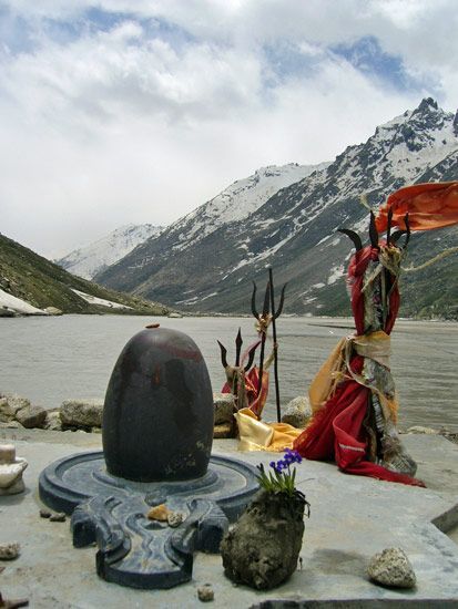 some statues are sitting on the edge of a body of water with mountains in the background