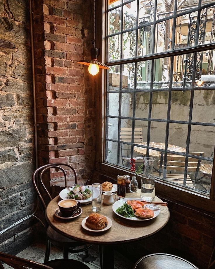 a table with plates of food on it in front of a brick wall and window