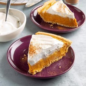 two slices of pumpkin pie on purple plates with whipped cream in the bowl behind them