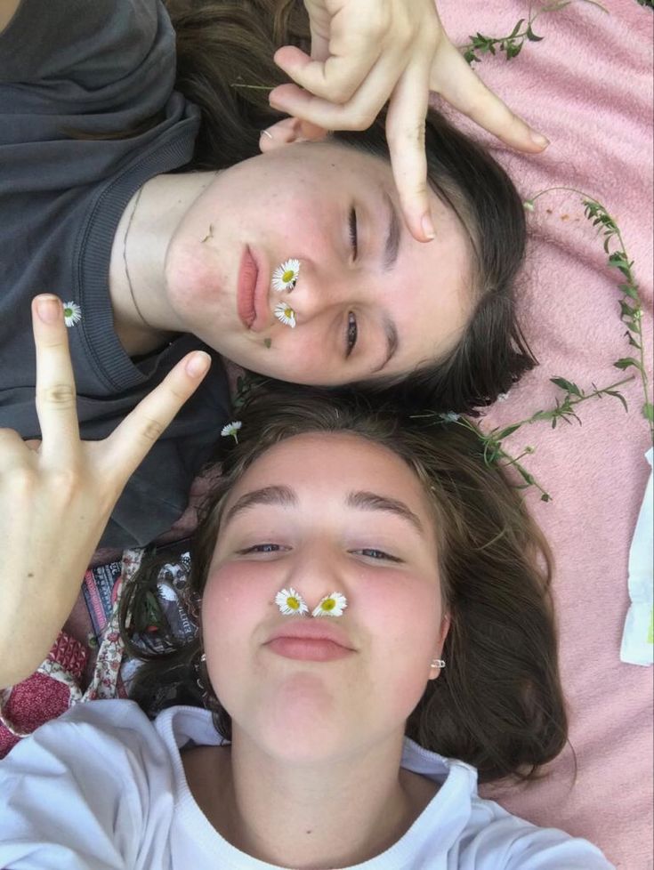 two people laying on top of each other with their fingers in the air and flowers painted on their eyes