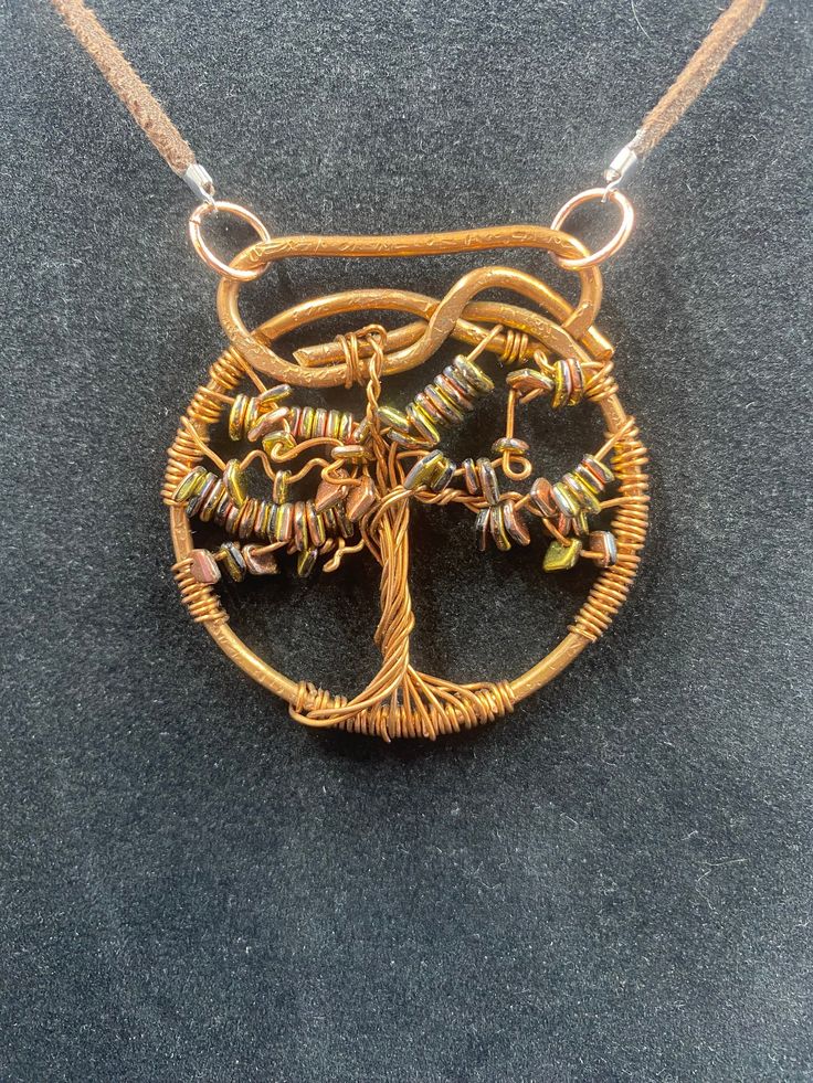 a necklace made out of wire with a tree on the front and bottom, sitting on a black surface