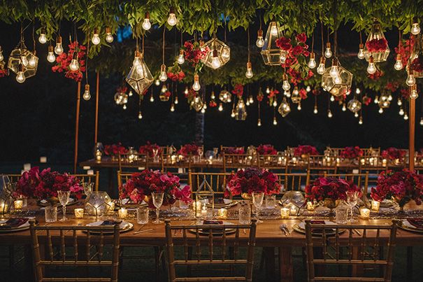 an outdoor dinner table set up with candles and flower centerpieces, surrounded by greenery