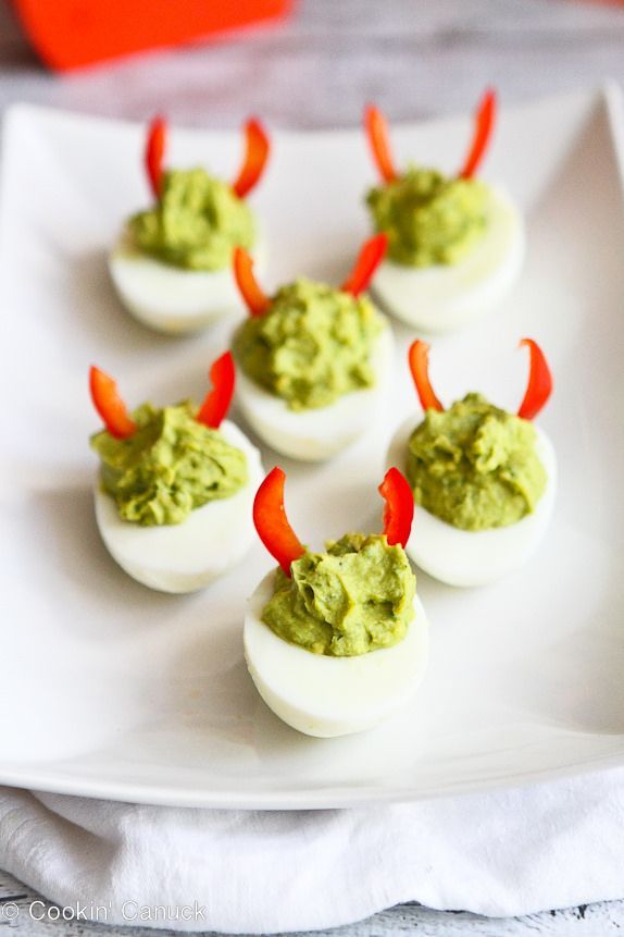 deviled eggs with red peppers and guacamole on a white platter