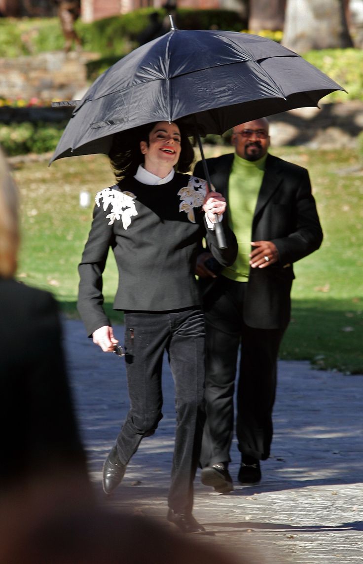 a woman holding an umbrella while walking down the street with another person behind her and one man standing next to her