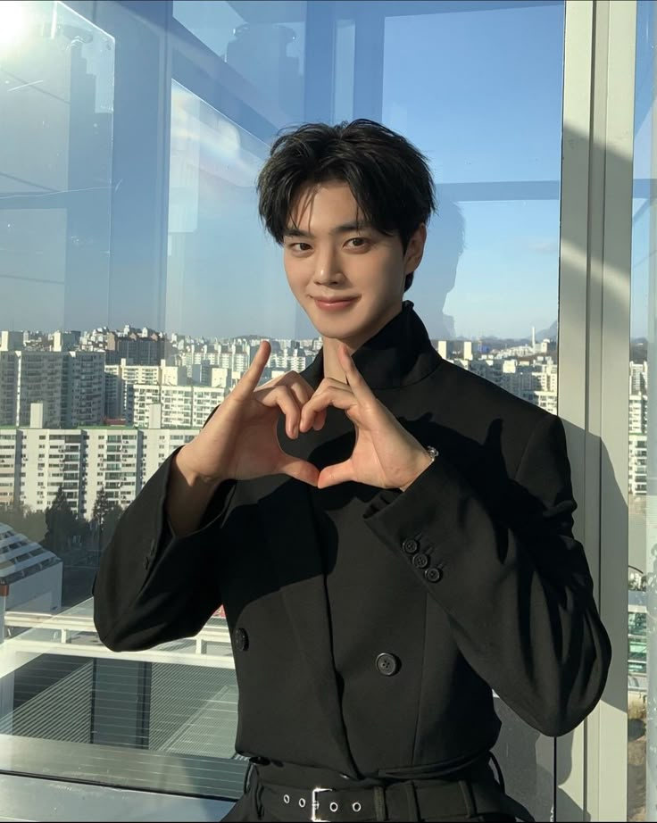 a young man making a heart with his hands while standing in front of a window