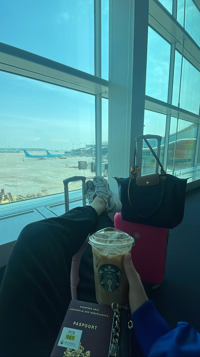 a woman sitting in an airport terminal with her hand on a starbucks drink and looking out the window