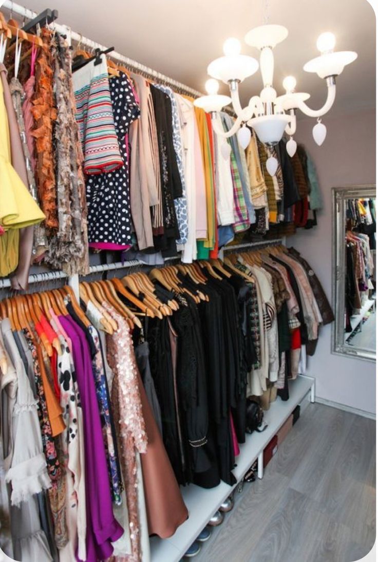 a closet filled with lots of clothes and clothing hanging on shelves next to a chandelier