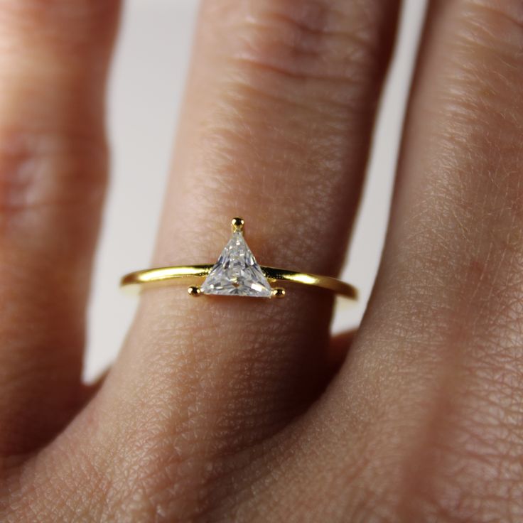 a woman's hand wearing a gold ring with a white diamond in the middle