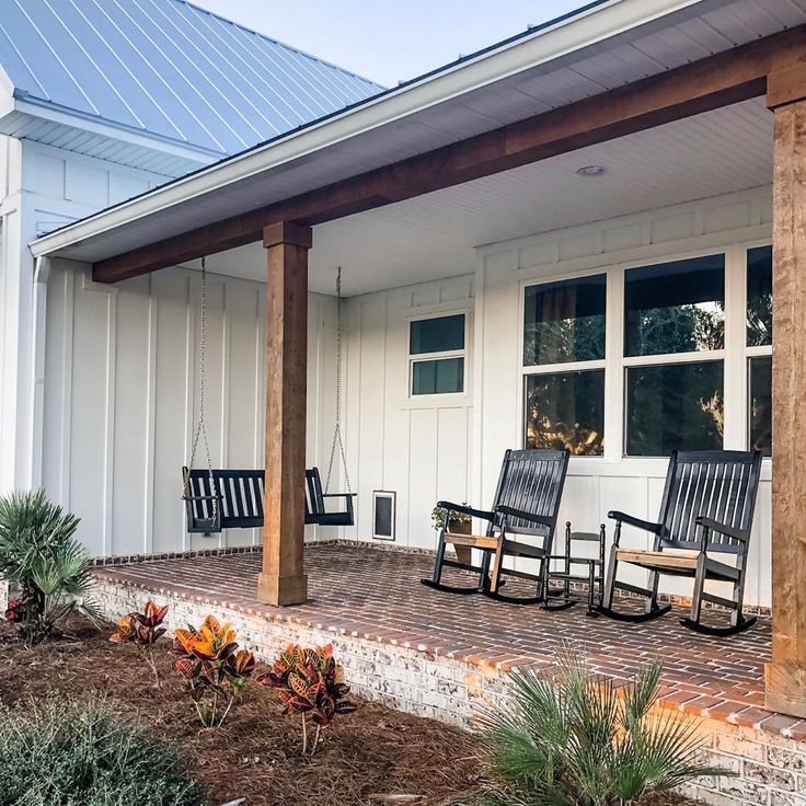 two rocking chairs on the front porch of a white house with wood columns and brick flooring