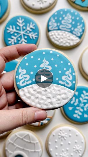 someone is holding some decorated cookies in front of a white and blue background with snowflakes