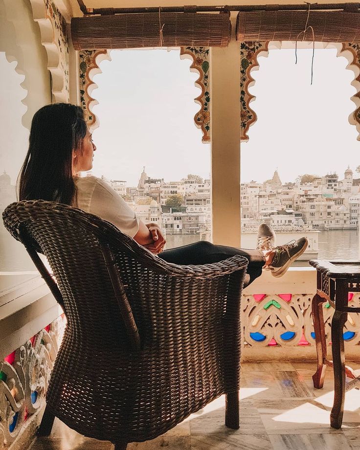 a woman sitting in a wicker chair looking out at the city from her balcony