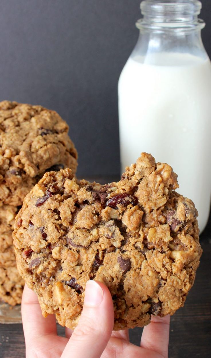 two cookies are being held in front of a glass of milk on a wooden table