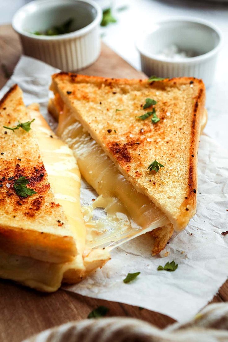 two grilled cheese sandwiches sitting on top of a wooden cutting board