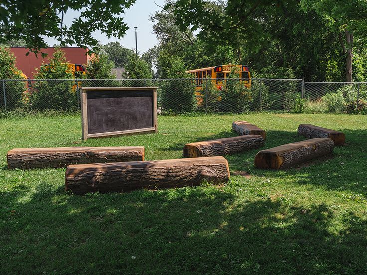 some logs that are in the grass near a fence and tree stumps with a chalkboard on them