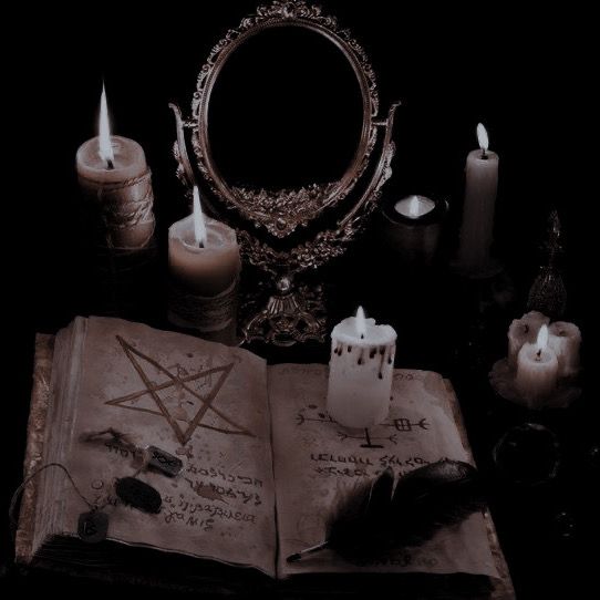 an open book sitting on top of a table next to some candles and a mirror