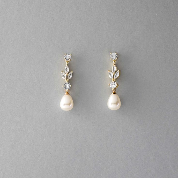 two pairs of pearl and diamond earrings on a gray surface, one with a single drop