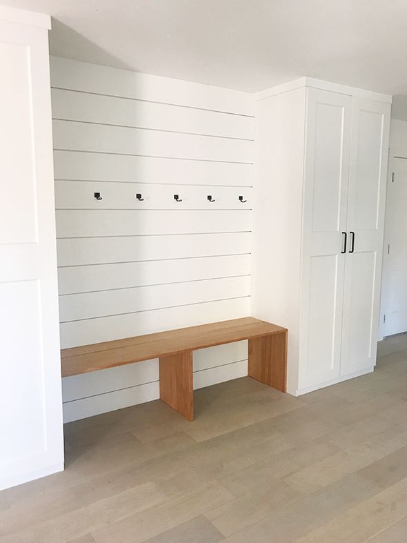 an empty room with white walls and wooden bench in the center, on hard wood flooring