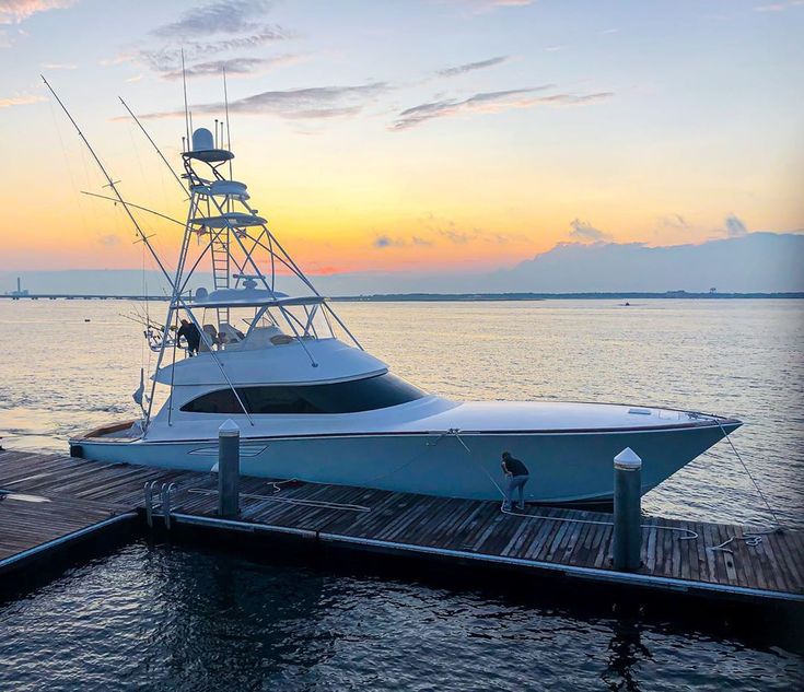 a boat is docked at the end of a pier as the sun sets in the background