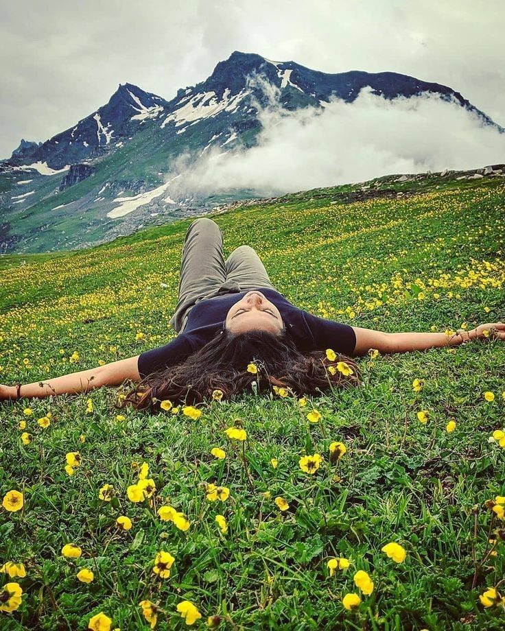 a woman laying in the grass with her head on her hands and eyes closed, surrounded by yellow flowers