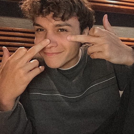 a young man holding his fingers up to the side and making a peace sign with his hand