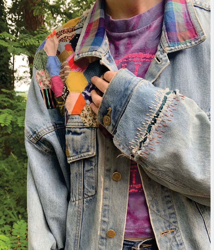 a woman wearing a jean jacket and colorful scarf around her neck, with trees in the background