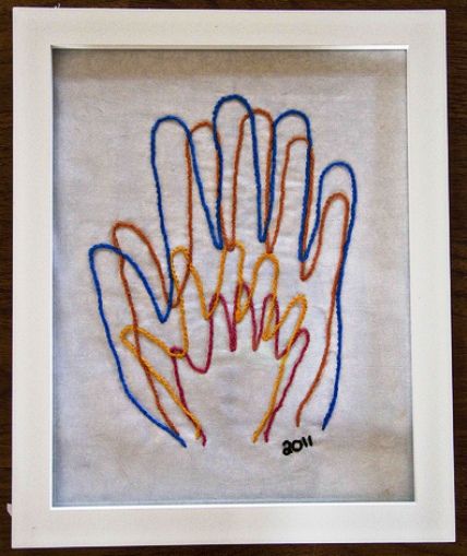 an embroidered handprint in a white frame on a wooden table with a brown background