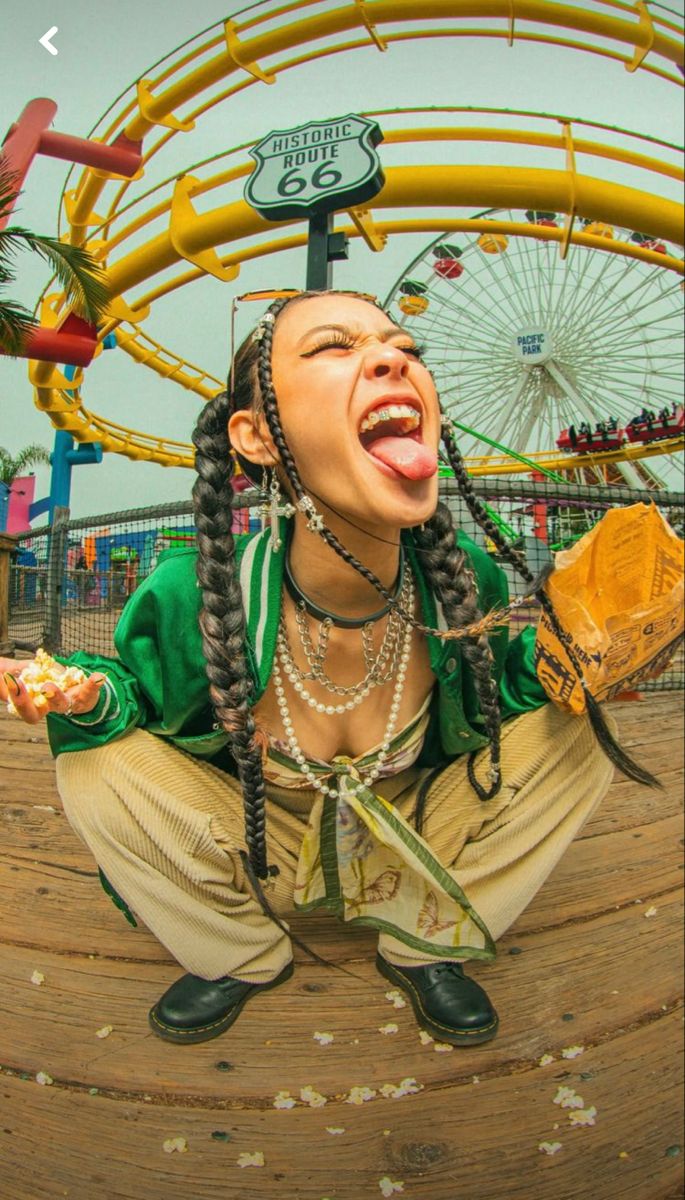 a woman with dreadlocks sitting on the ground in front of a carnival ride