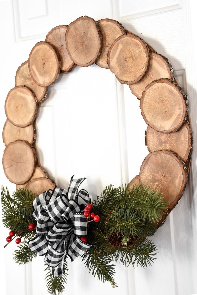 a wreath made out of logs and pine branches with a bow hanging on the front door