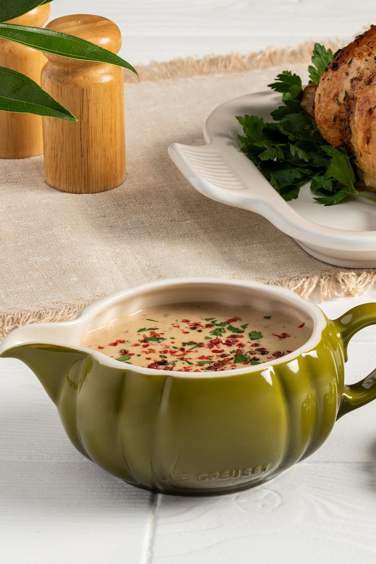 a green pitcher filled with soup sitting on top of a table next to a plate of food