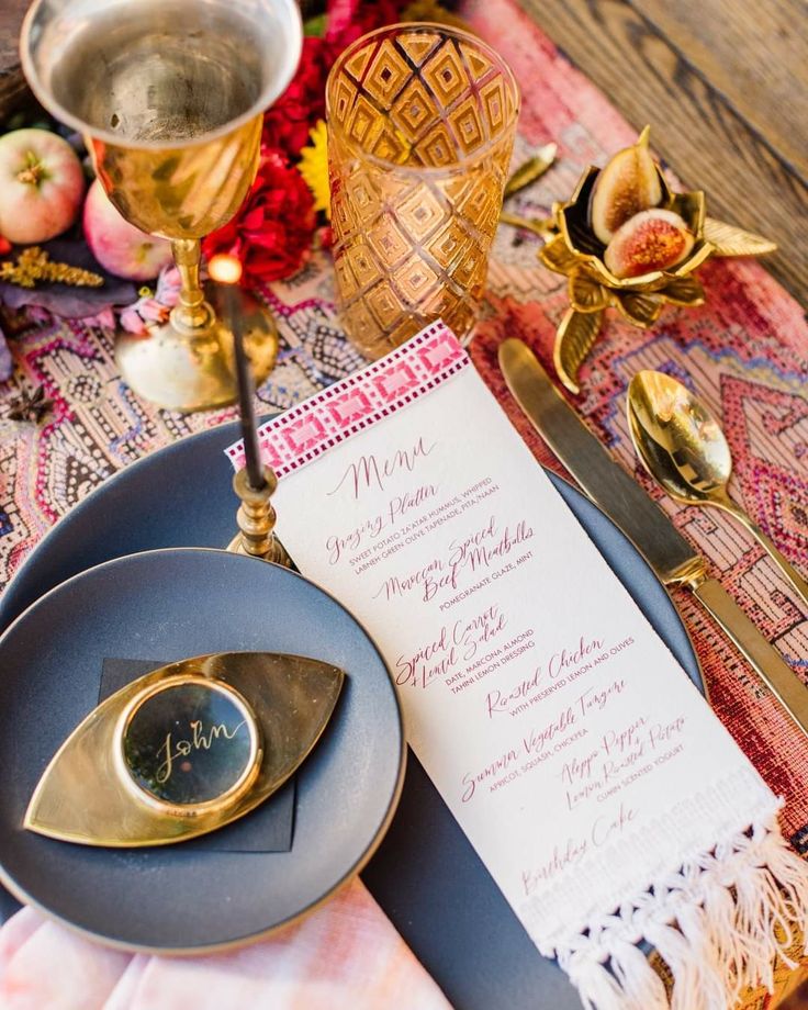 a table setting with menus and silverware on it, including an ornate vase