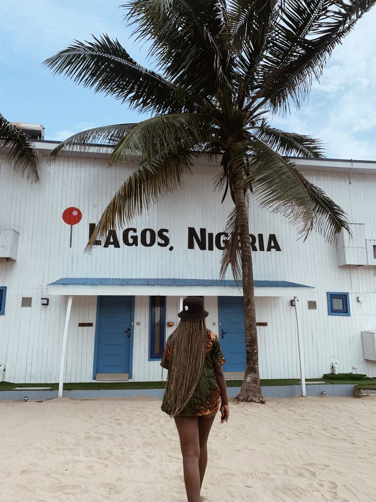 a woman standing under a palm tree in front of a white building with blue doors