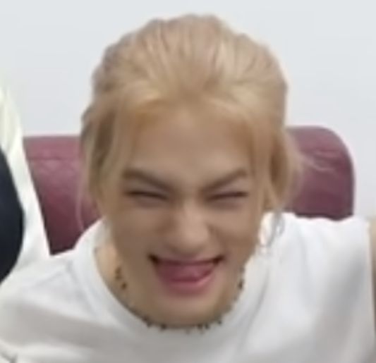 a man with blonde hair wearing a white shirt and smiling at the camera while sitting on a couch