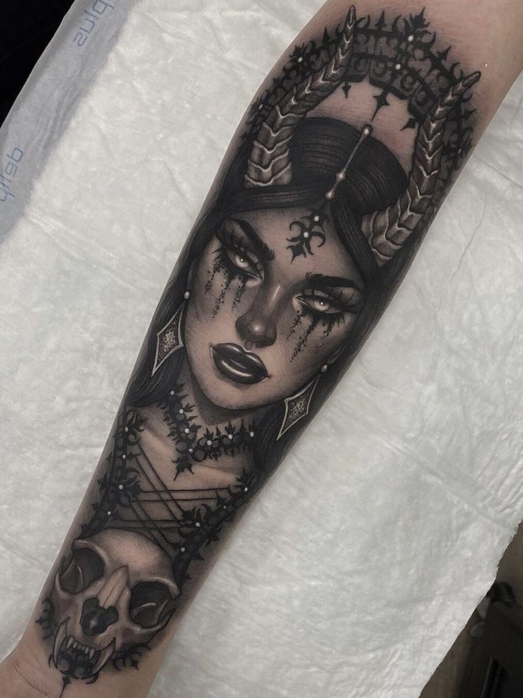 a woman's face and skull tattoo on the left arm, with an elaborate wreath around her head