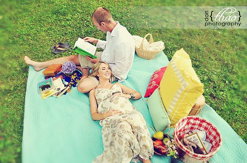 a man and woman laying on a blanket in the grass with picnic items around them