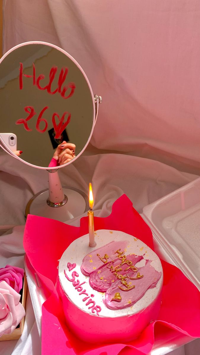 a birthday cake sitting on top of a pink napkin next to a mirror with writing on it