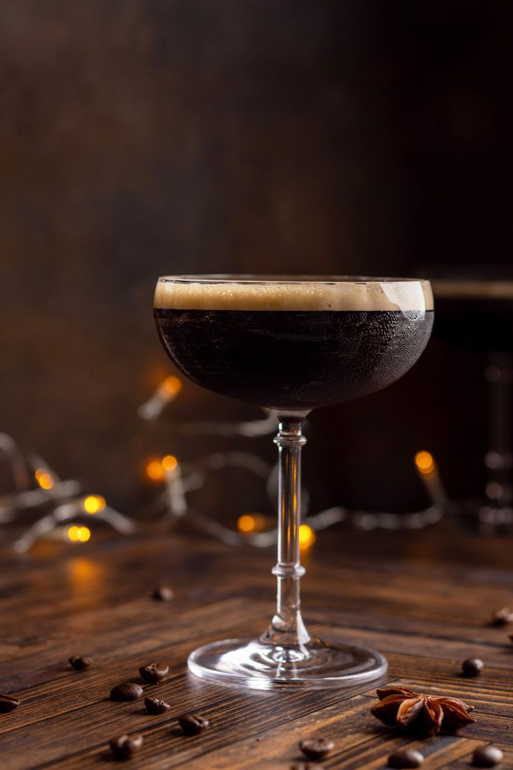 a glass filled with liquid sitting on top of a wooden table next to coffee beans