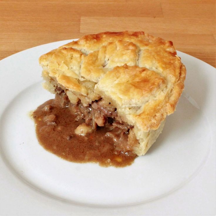 a piece of meat pie on a white plate with gravy and brown sauce