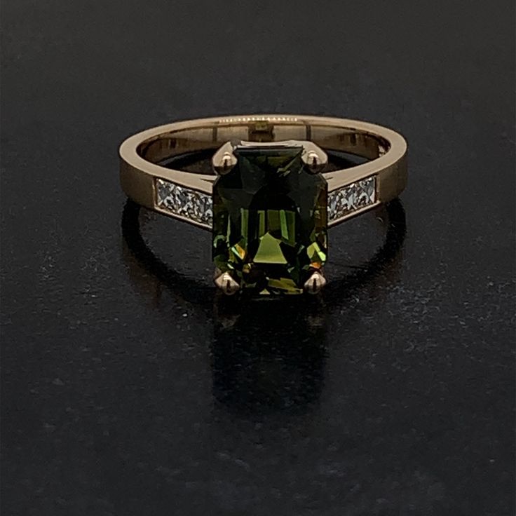 This is a very special one of a kind ring that is set in 14 karat yellow gold. The center stone is a Rare Natural Ceylon Green Sapphire with no indication of heat applied. This specialty mixed cut stone has a deep green tone with shades of soft yellow as well. The hardness on this stone is a 9 out of 10 on the Mohs scale. It weighs 3.25 carats and is surrounded by 6 Natural French Cut Square Diamonds weighing 0.26 carats total weight and the stones are graded G in color and VS2 in Clarity. These Modern Green Jewelry With Accent Stones, Green Princess Cut Diamond Ring In 14k Gold, 14k Gold Green Diamond Princess Cut Ring, Modern Green Emerald Ring With Accent Stones, Modern Emerald-cut Green Diamond Ring, Princess Cut Green Diamond Ring In 14k Gold, Modern Green Rings With Prong Setting, Luxury Green Radiant Cut Rings, Timeless Green Rings With Accent Stones