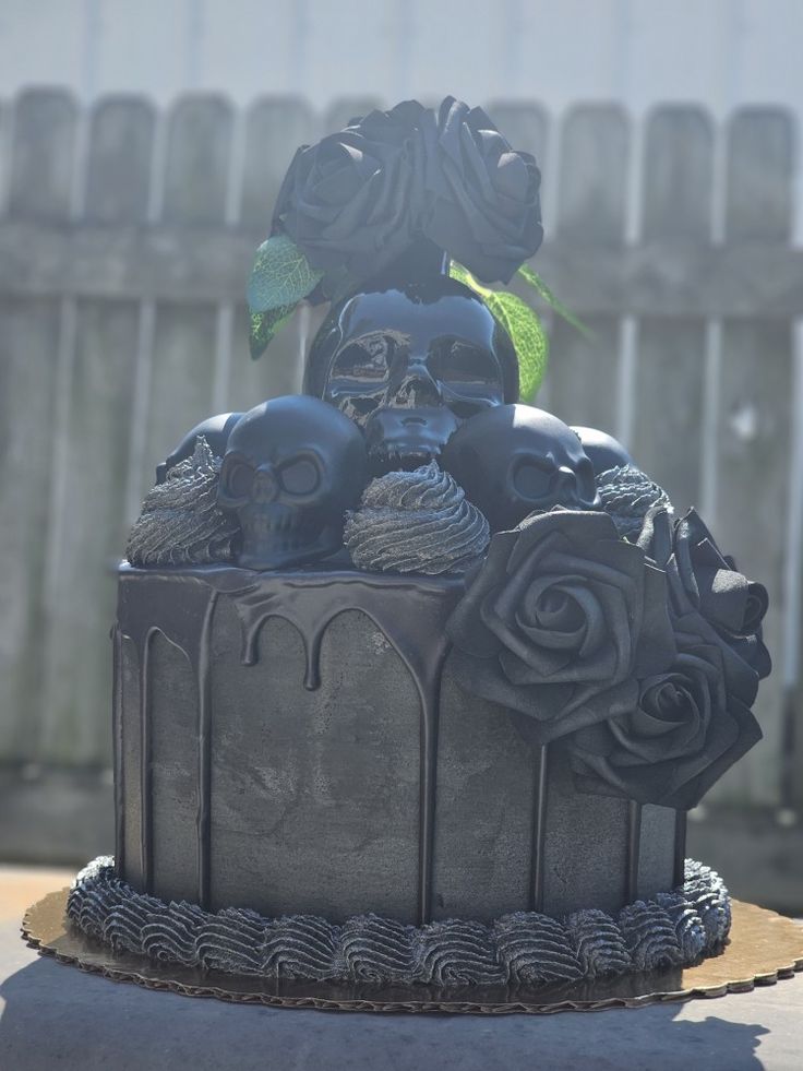 a black cake with skulls and roses on it's top is sitting in front of a fence