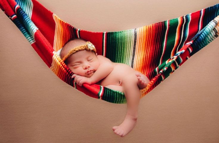 a baby sleeping in a colorful hammock on top of a brown wall with a tan background