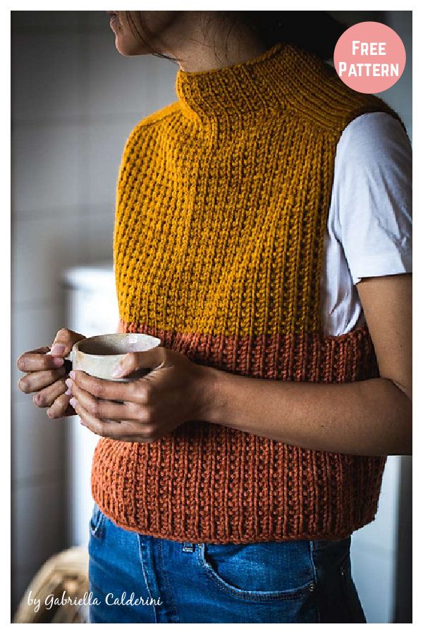 a woman holding a cup in her hands while wearing a knitted sweater and jeans