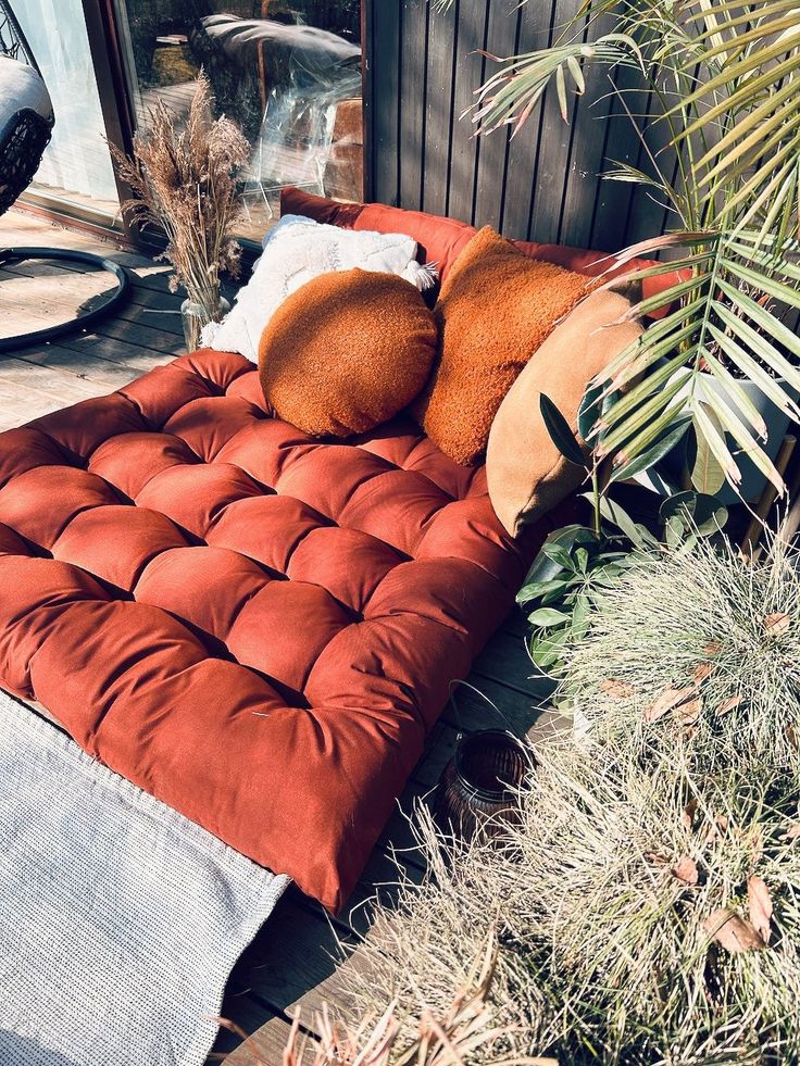 a red couch sitting on top of a wooden floor next to plants and bushes in front of a building