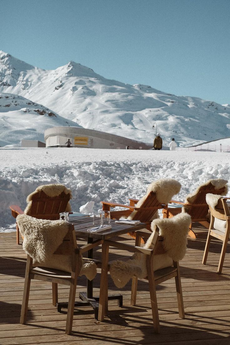 two chairs and a table on a deck with snow covered mountains in the background