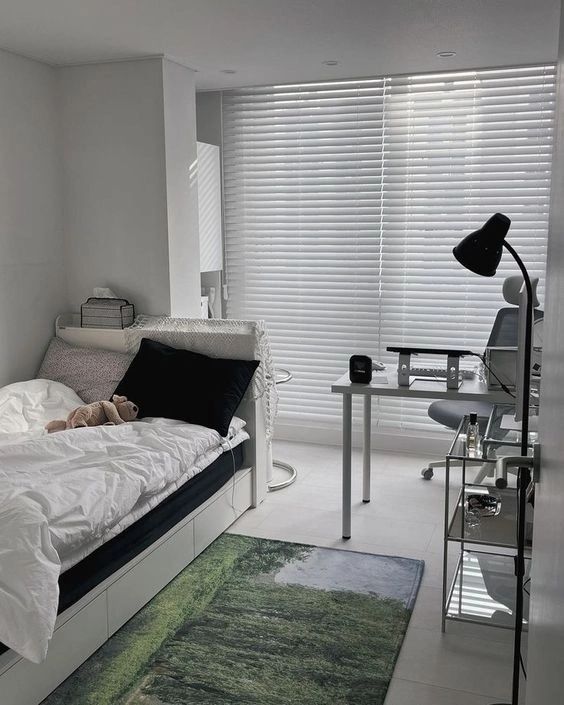 a bedroom with a bed, desk and computer on the floor in front of a window