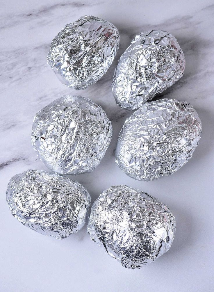 four pieces of silver foil sitting on top of a white marble countertop next to each other