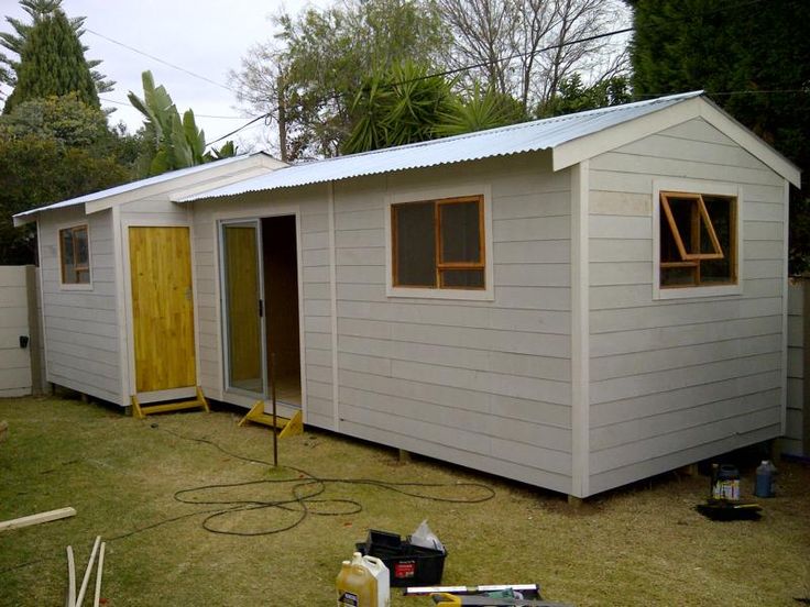 a small white shed sitting on top of a grass covered yard next to a fence