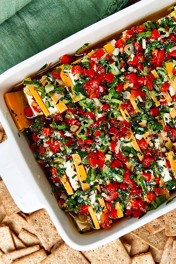 a casserole dish with tomatoes, cheese and spinach in it on top of crackers