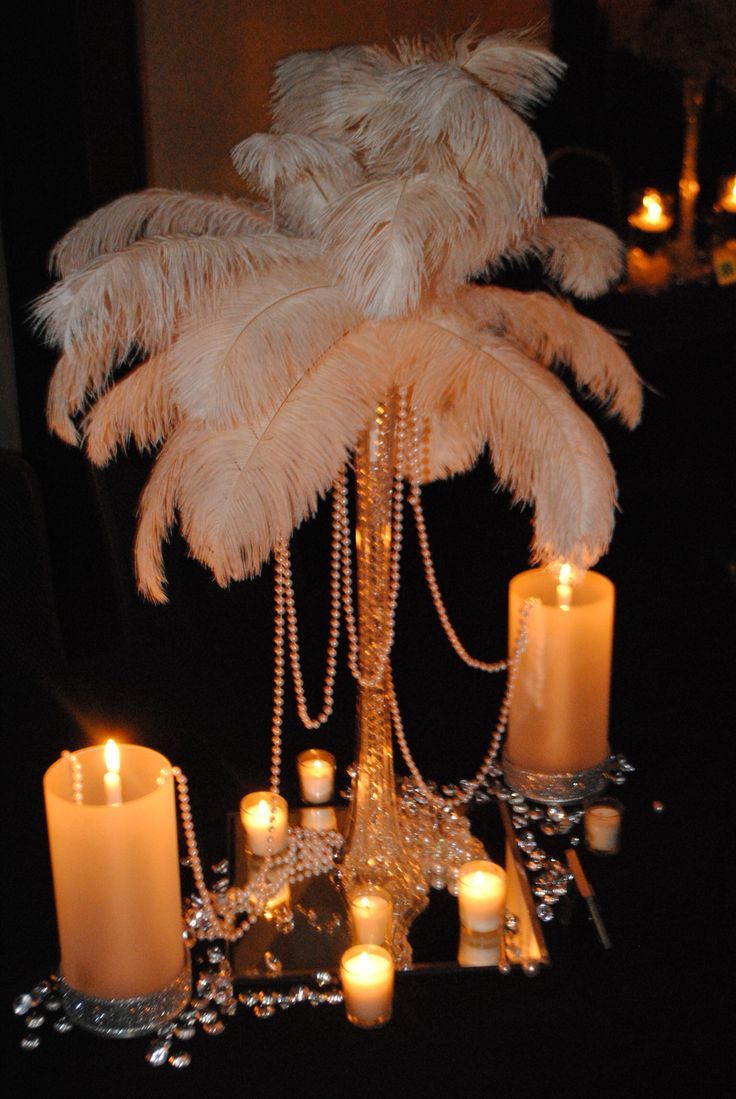 a table topped with candles and a tall palm tree covered in feathers on top of it