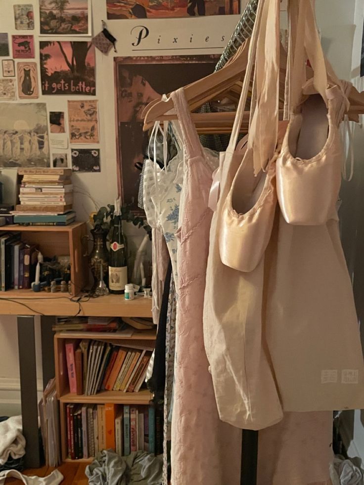 three women's handbags hanging from clothes racks in a room with bookshelves